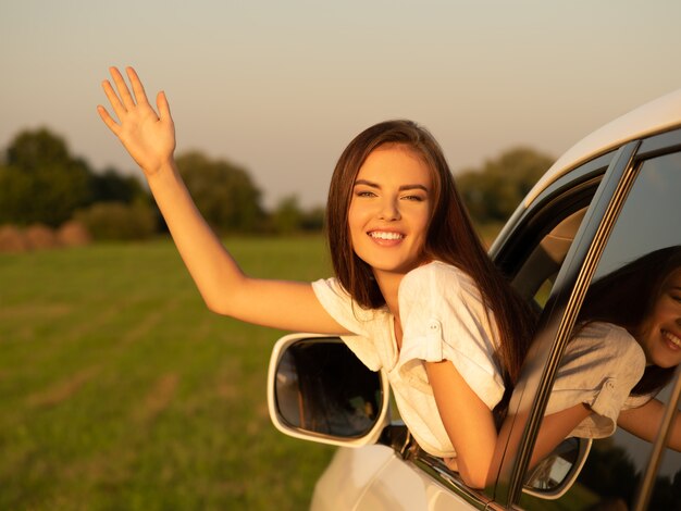 Mujer feliz en el coche con la mano levantada.