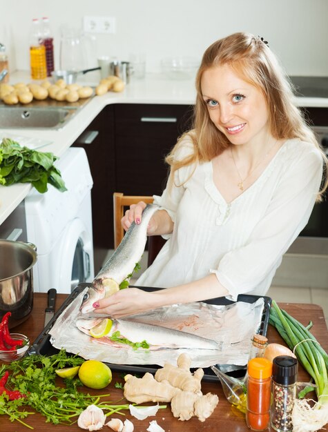 Mujer feliz cocinando pescado con limón en una sartén