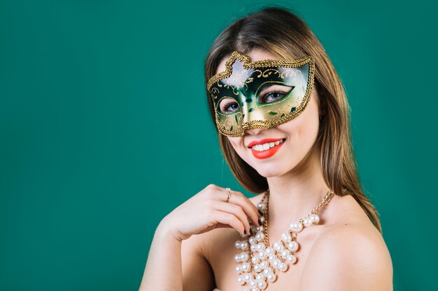 Mujer feliz con el collar de los granos que lleva la máscara del carnaval de la mascarada en fondo verde