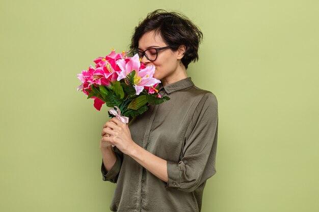 Mujer feliz y complacida con el pelo corto con ramo de flores y oliendo