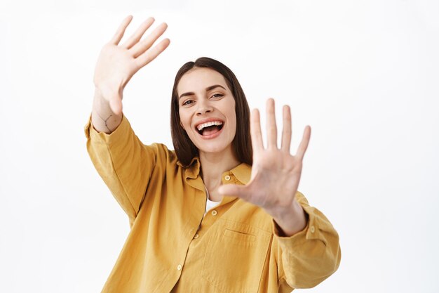 Mujer feliz creativa estirar las manos soñadoras, sonriendo y riendo sin preocupaciones, haciendo gestos de marcos de mano, ampliar sus puntos de vista, explorar algo nuevo, de pie sobre fondo blanco