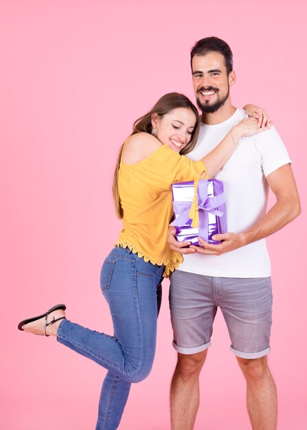 Mujer feliz dando un abrazo a su novio con regalos envueltos sobre fondo rosa