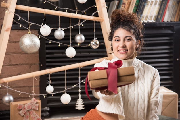 Una mujer feliz dando una caja de regalo con lazo.