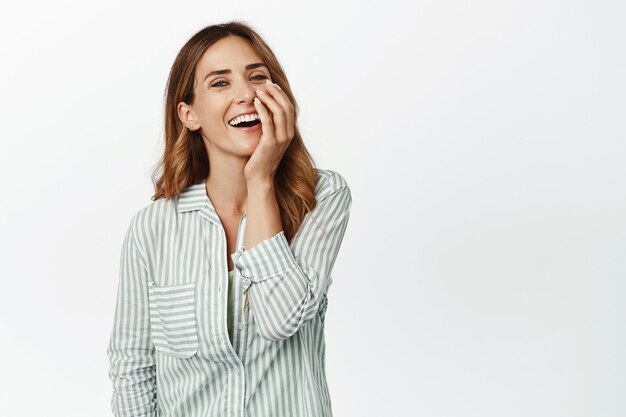 Mujer feliz despreocupada en blusa, riendo y sonriendo alegre, tocando la cara y mirando optimista al frente