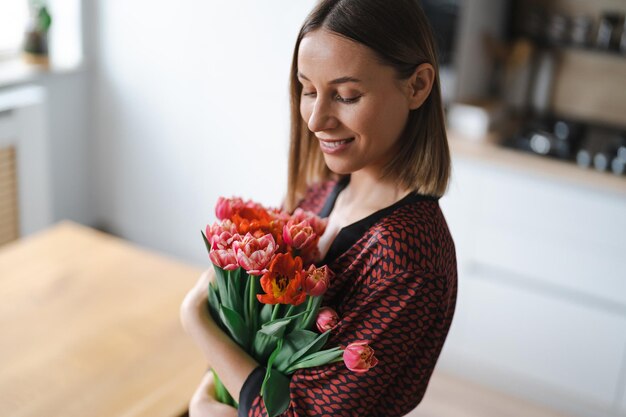 Mujer feliz disfruta de un ramo de tulipanes Ama de casa disfrutando de un ramo de flores y el interior de la cocina Dulce hogar Libre de alergias