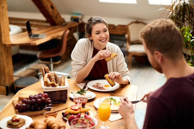 Mujer feliz disfrutando de una conversación con su novio durante el desayuno en la mesa de comedor