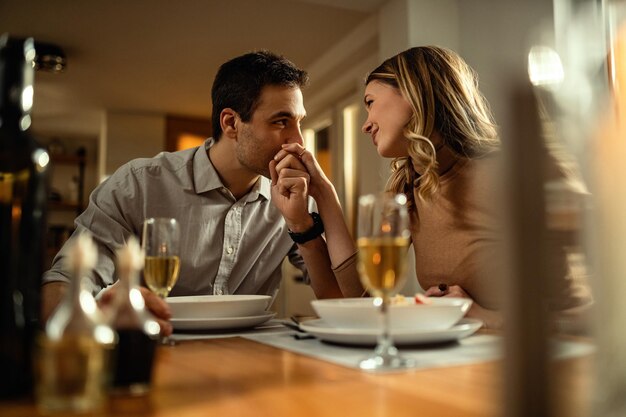Mujer feliz disfrutando en la mesa del comedor mientras su novio la besa en la mano