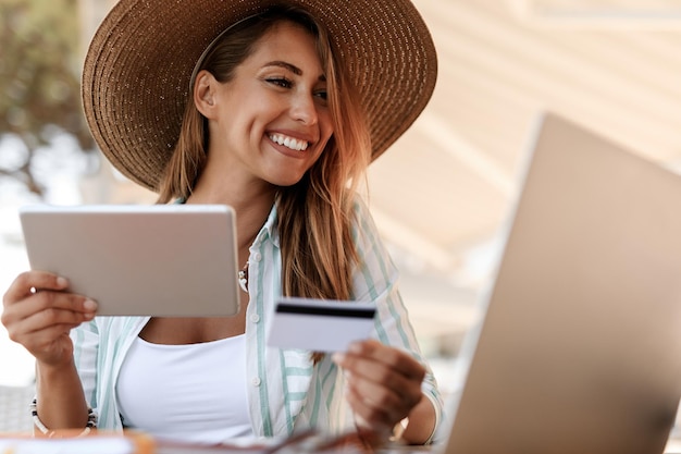 Mujer feliz ebanking con tarjeta de crédito mientras usa el panel táctil y la computadora portátil en un café