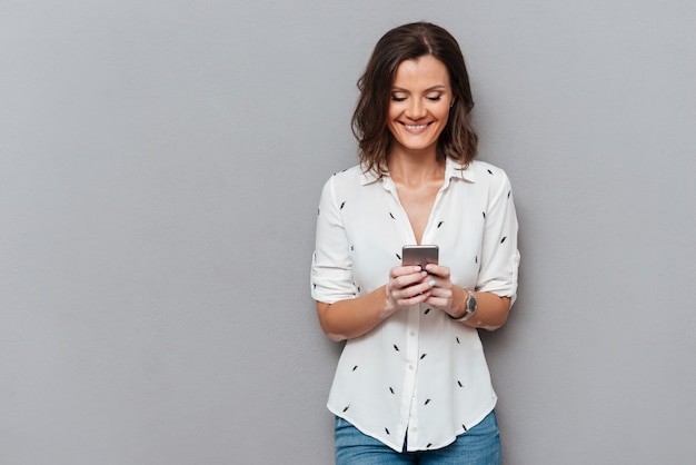 Foto gratuita mujer feliz escribiendo mensajes en su teléfono inteligente en gris