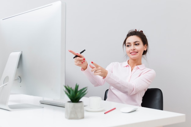 Mujer feliz en el escritorio apuntando a la computadora