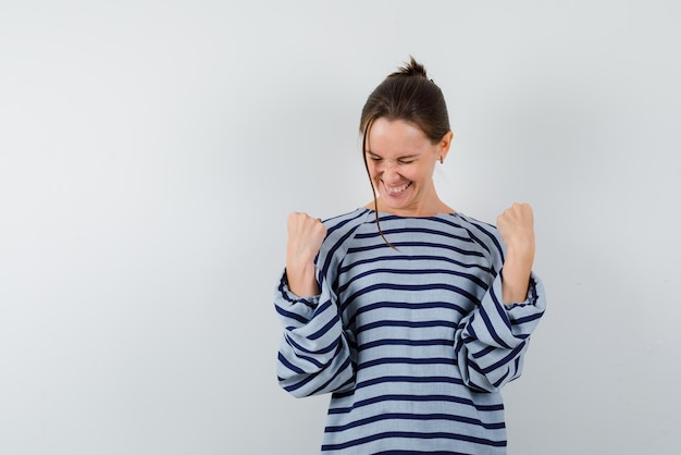 La mujer feliz se está apretando los puños sobre fondo blanco.