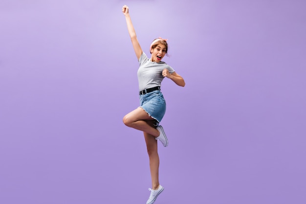 Mujer feliz en falda y camisa salta sobre fondo morado. Chica joven alegre de buen humor en traje elegante posando.n telón de fondo aislado.