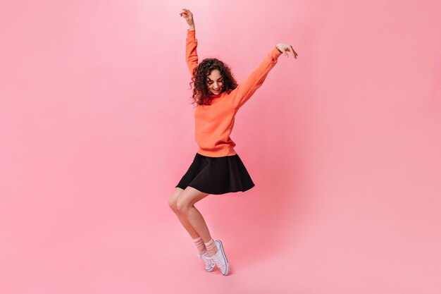 Mujer feliz en falda negra y suéter posando sobre fondo rosa