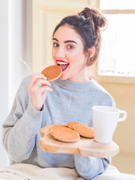 Mujer feliz en gris comiendo galletas