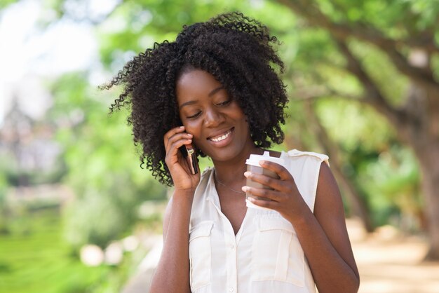 Mujer feliz hablando por teléfono y bebiendo café