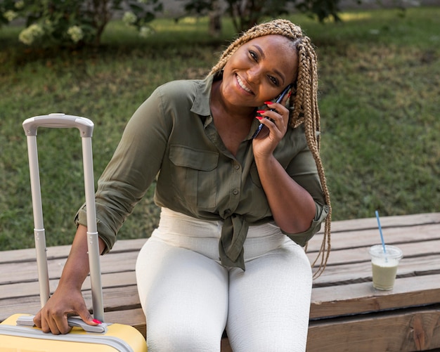 Mujer feliz hablando por teléfono mientras sostiene su equipaje