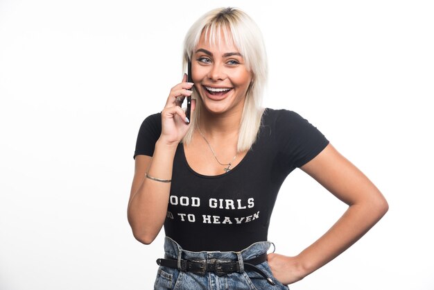 Mujer feliz hablando por teléfono en la pared blanca.