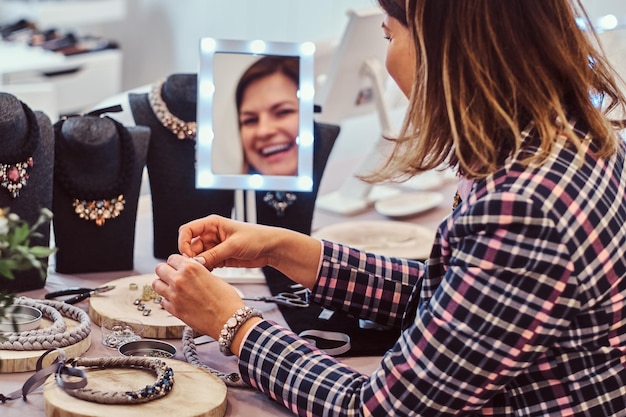 Foto gratuita mujer feliz hace collares hechos a mano, trabajando con agujas e hilo en taller de joyería.