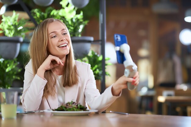 Mujer feliz haciendo selfie con teléfono moderno en café