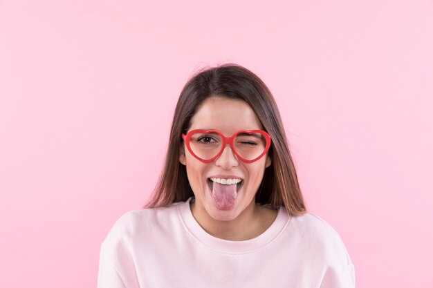 Mujer feliz joven con las lentes que muestran la lengua