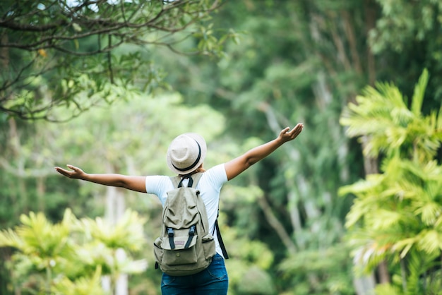 La mujer feliz joven con la mochila que levanta la mano goza con la naturaleza.