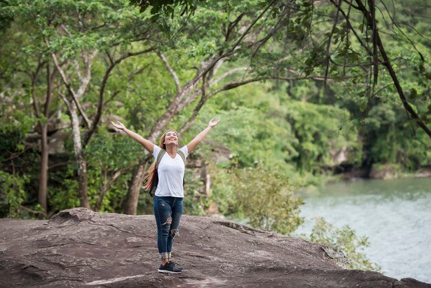 La mujer feliz joven con la mochila que levanta la mano goza con la naturaleza.