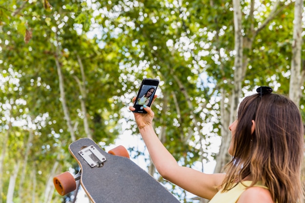 Mujer feliz joven con el monopatín que toma el selfie