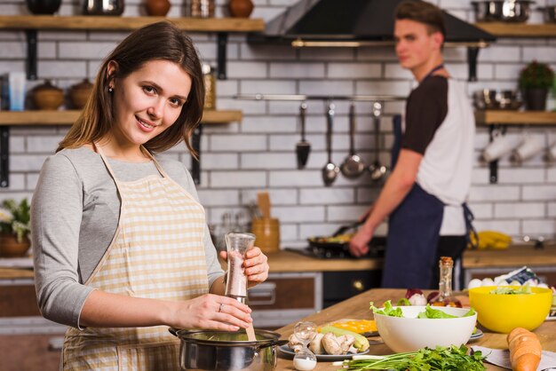 Mujer feliz joven con el novio que cocina en cocina