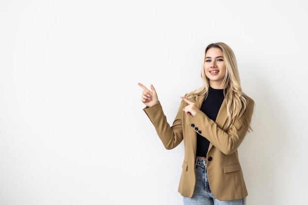 Mujer feliz joven sorprendida que señala el fondo blanco de pie fascinado