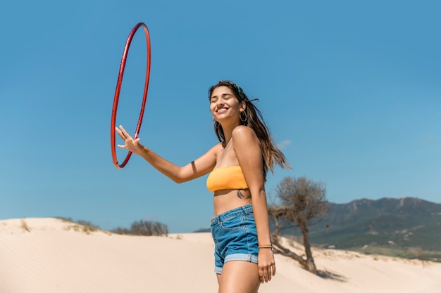 Mujer feliz jugando con el aro de hula en la arena