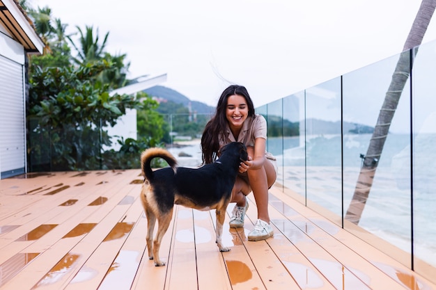 Mujer feliz jugando con perro en terraza con paisaje marino