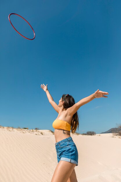 Mujer feliz lanzando hula hoop y caminando sobre la arena