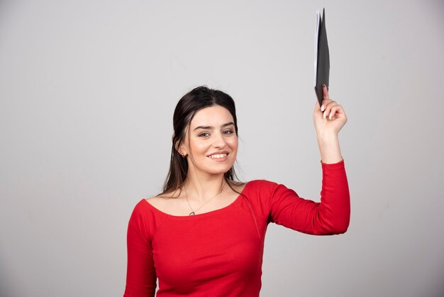 mujer feliz con lápiz y portapapeles sobre un fondo gris.