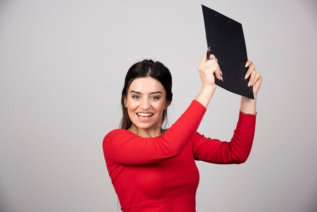 mujer feliz con lápiz y portapapeles sobre un fondo gris.