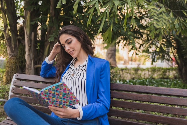 Mujer feliz leyendo un cuaderno en un banco del parque