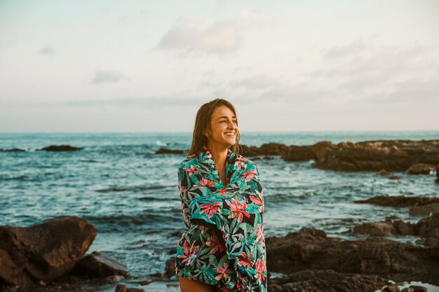 Mujer feliz en manta de pie en la orilla del mar