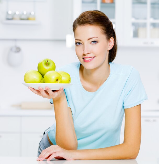 Mujer feliz con manzanas verdes en un plato en la cocina