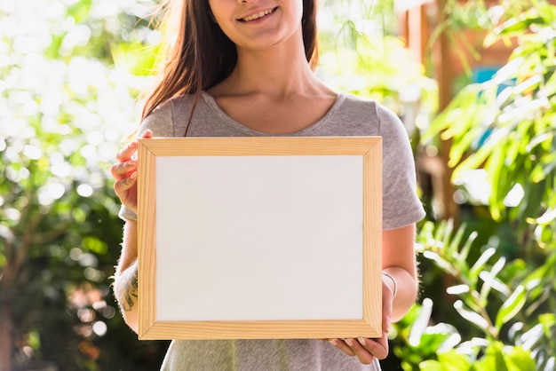 Mujer feliz con marco de foto entre plantas