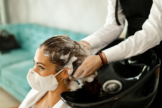 Mujer feliz con mascarilla protectora disfrutando en la peluquería durante la epidemia de coronavirus