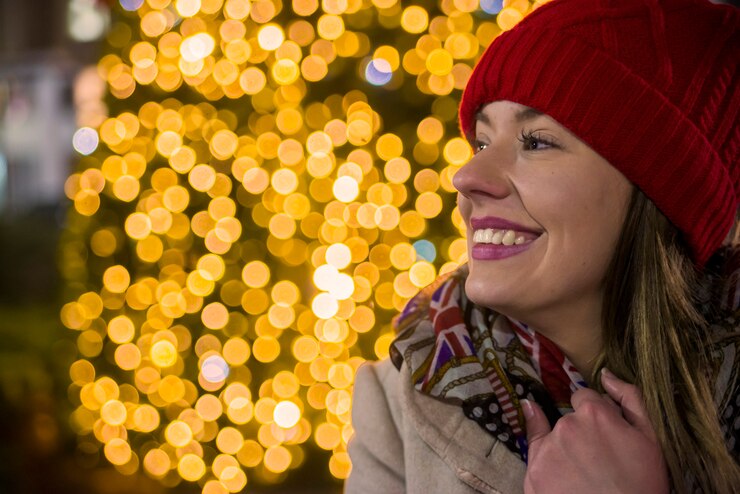Mujer feliz mirando hacia arriba con la luz de Navidad en la noche. Muchacha feliz en la calle adornada para la Navidad que mira para arriba