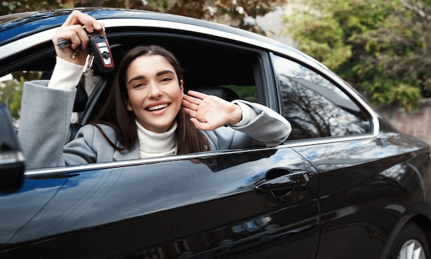 Mujer feliz mirando por la ventana y mostrando las llaves del coche nuevo, compró un nuevo automóvil