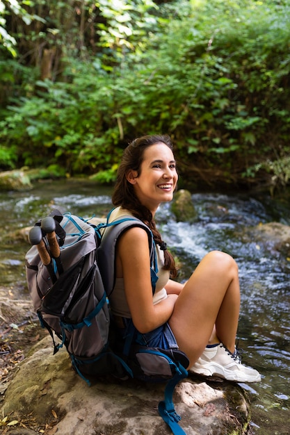 Foto gratuita mujer feliz con mochila descansando mientras explora la naturaleza