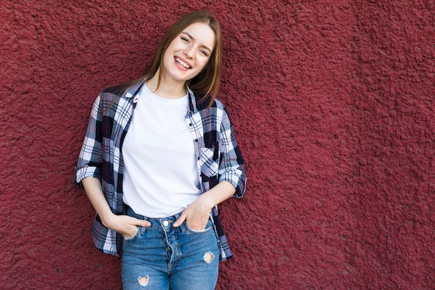 Mujer feliz de moda que se inclina en la pared texturizada roja