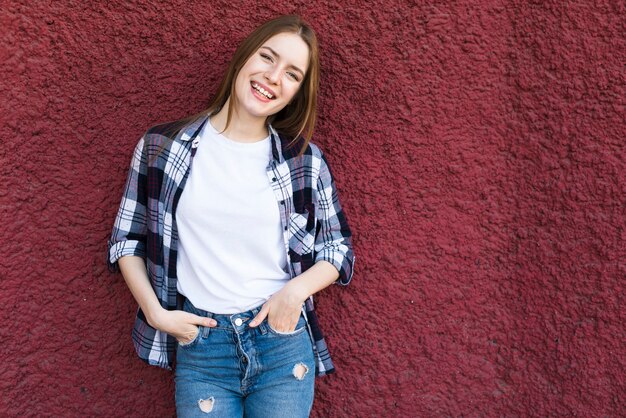 Mujer feliz de moda que se inclina en la pared texturizada roja