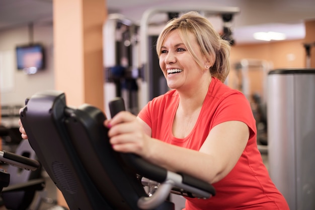 Mujer feliz montando en bicicleta estática en el gimnasio