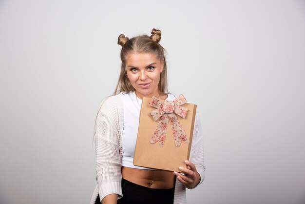 Mujer feliz mostrando caja de regalo de vacaciones en la pared gris.