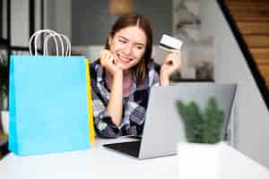 Foto gratuita mujer feliz mostrando tarjeta de crédito y mirando portátil