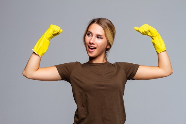 Mujer feliz mostrar bíceps poniéndose guantes protectores amarillos en gris aislado. Concepto de limpieza