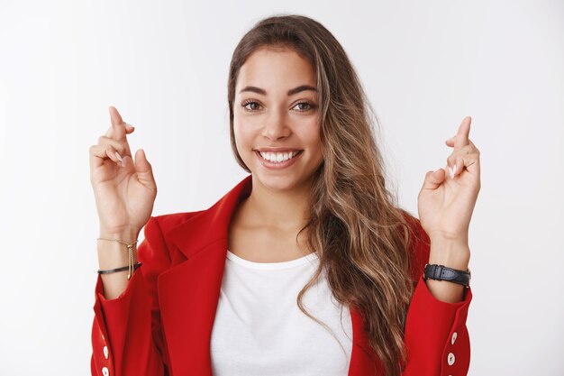 Mujer feliz optimista haciendo deseo sonriendo éxito dirigido, dedos cruzados buena suerte sonriendo mirando cámara esperanzada emocionada, esperando resultados positivos, rezando soñando deseo hecho realidad, pared blanca