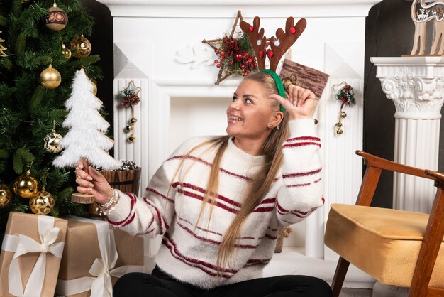 Mujer feliz en orejas de ciervo apuntando al árbol de juguete.